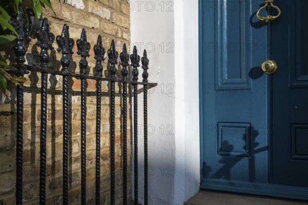 Blue door with brass-coloured door handle and wrought-iron grille in the sunlight, Kensington, London, England, Great Britain