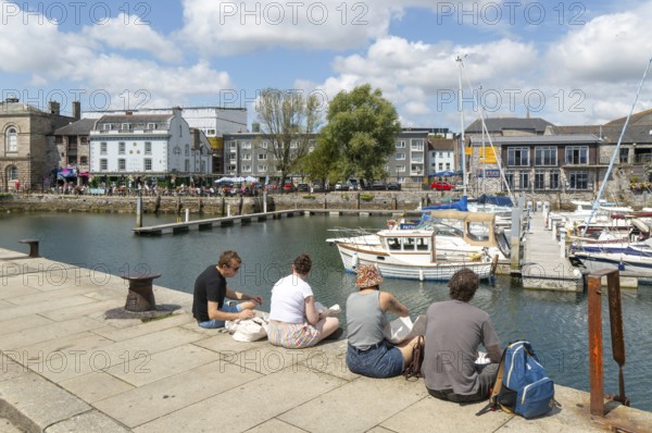 People sitting on quayside of marina harbour, The Barbican, Plymouth, Devon, England, UK