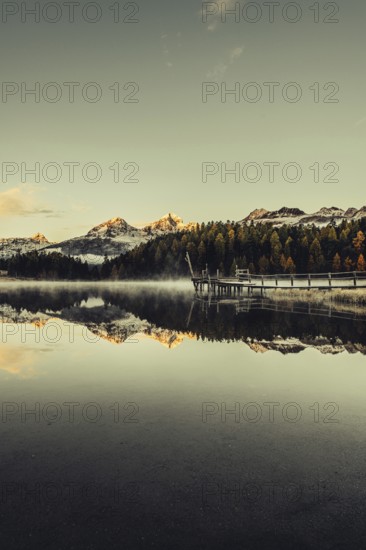Lake Staz near Sankt Moritz in the Engadin in Switzerland. Morning atmosphere with fog in autumn. Water reflection and snow-covered mountains in the background