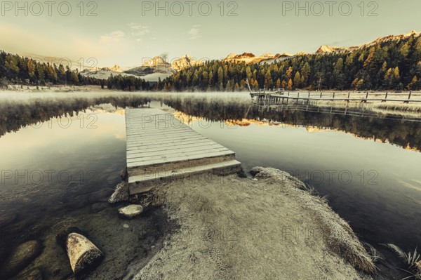 Lake Staz near Sankt Moritz in the Engadin in Switzerland. Morning atmosphere with fog in autumn. Water reflection and snow-covered mountains in the background