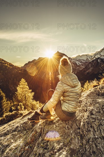 Woman sitting thoughtfully at a feslen at autumn atmosphere during sunset in the Swiss Alps in the Engadine. Photographed from the village of Maloja on the Maloja Pass