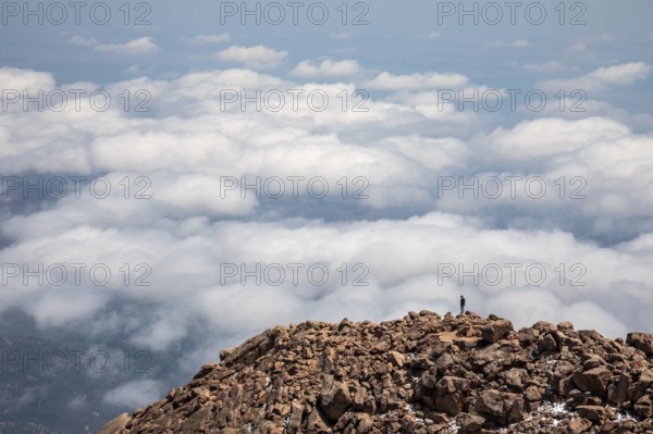 Colorado Springs, Colorado - A man stands on the rocks just below the summit of Pikes Peak, a 14, 115' mountain in Colorado's front range. Thousands of tourists visit, most by driving a steep road to the summit, or riding on a cog railway