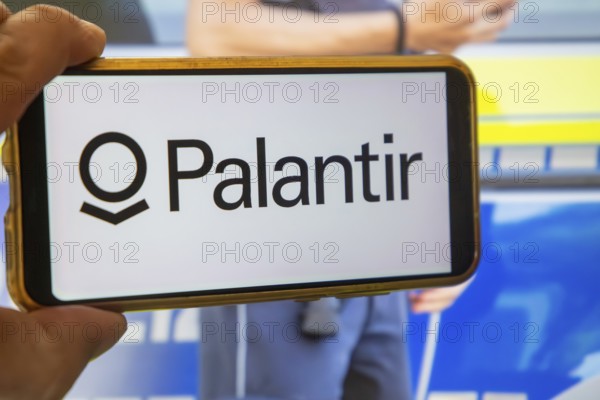 (Photomontage) Palantir symbolic image: PALANTIR logo on a smartphone, a police officer in the background