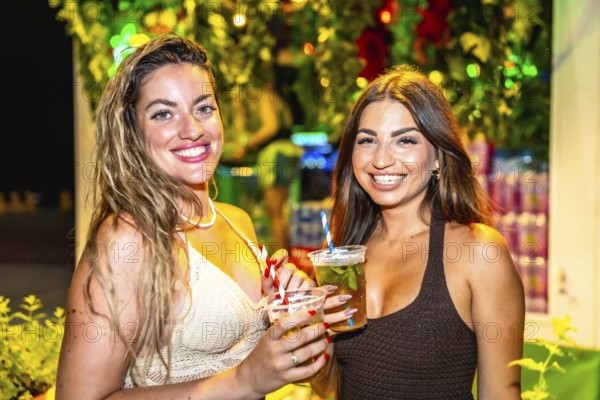 Two beautiful women enjoying cocktails at a summer night party, celebrating and having fun together