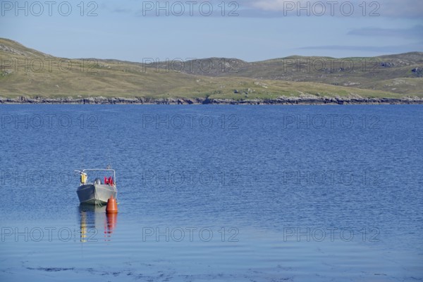 Lonely boat next to buoy on calm water, hilly landscape behind under clear sky, Hillswick, Eshaness, Shetland Islands, Scotland, United Kingdom