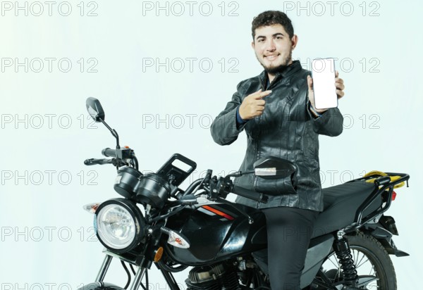 Young motorcyclist sitting on his motorcycle showing cell phone screen isolated. Male biker on his motorcycle showing phone screen