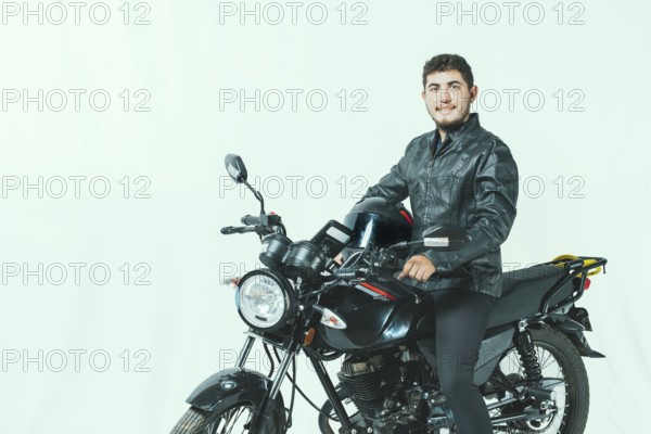 Smiling motorcyclist sitting on his motorcycle holding helmet, isolated. Portrait of handsome biker on motorcycle on isolated background