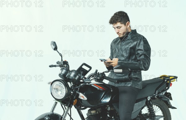 Young motorcyclist using his cell phone while sitting on his motorcycle, isolated. Male biker on a motorcycle using his phone isolated on white background
