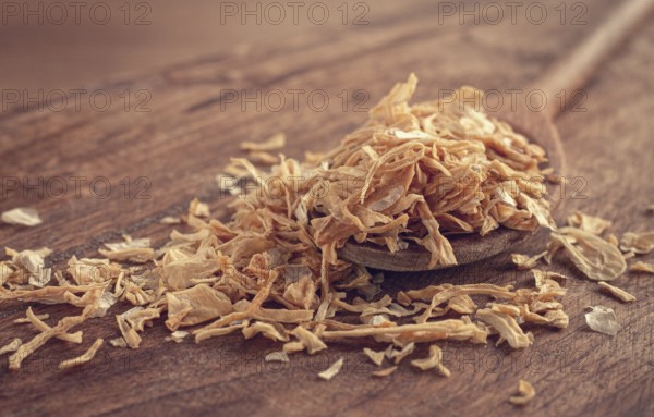 Smoked onion flakes, on a wooden spoon, wooden table, close-up