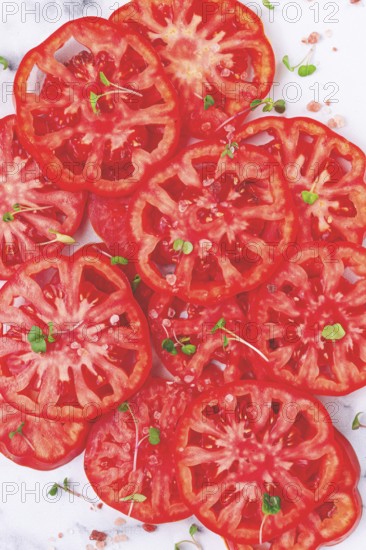 Freshly sliced ripe tomatoes arranged on a marble surface with microgreens and sea salt for a culinary presentation
