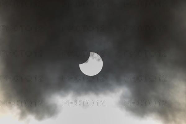 A partial solar eclipse occurs when the moon eclipses part of the sun and is surrounded by dynamic cloud formations. The event takes place during the day and offers an impressive visual experience. High Rhine, Vosges, Great East, France