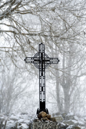 A beautiful wayside cross stands tall in winter with snow blanketing the landscape of the Aubrac plateau in Lozere, Occitanie. France