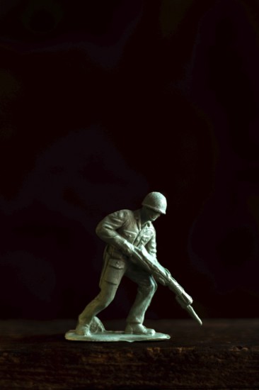 A small soldier figure stands ready with a rifle, capturing the essence of military readiness and attention to detail against a dark backdrop