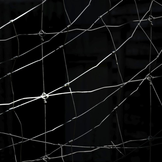 Worn netting stretches across a dark backdrop, showcasing intricate patterns and textures. The play of light and shadow emphasizes the delicate details of the material, creating depth