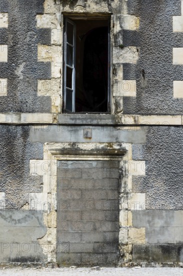 An abandoned structure stands with a weathered gray facade and an open window, highlighting urban neglect in a serene area. The building bears the marks of time and disrepair. France