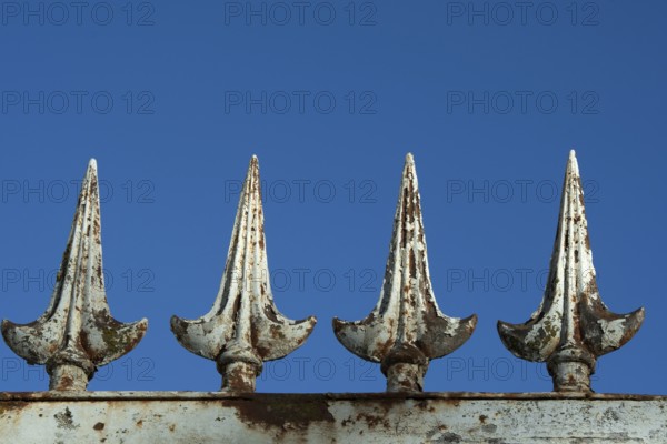 Four rusted metal spikes rise prominently against a vivid blue sky, showcasing weathered details that highlight their ornamental design and aged texture. France