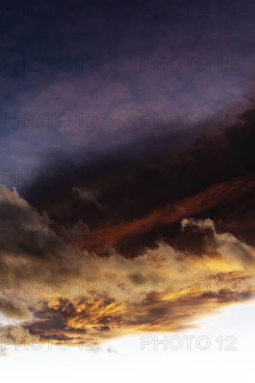 A stunning display of clouds during sunset showcases vibrant orange and deep purple colors fading into the night sky. The view captures nature's beauty in a tranquil moment of the day