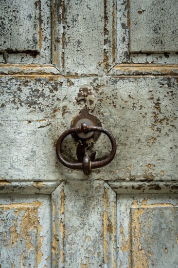 A close-up of a weathered wooden door surface reveals peeling paint and a vintage metal knocker. The texture tells a story of age and traditional craftsmanship