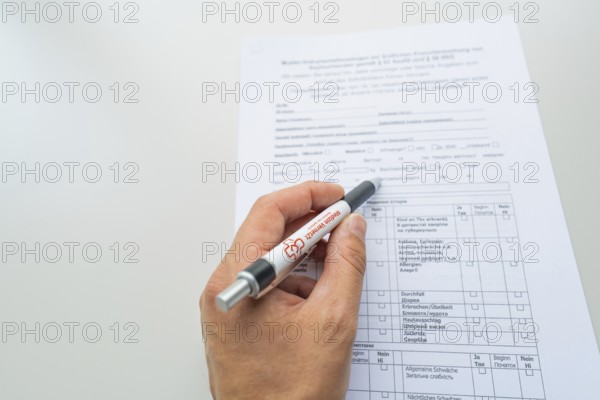 Hand holding a pen while filling out a form on the desk, Care Connect, vaccination kiosk for refugees, Calw, Germany