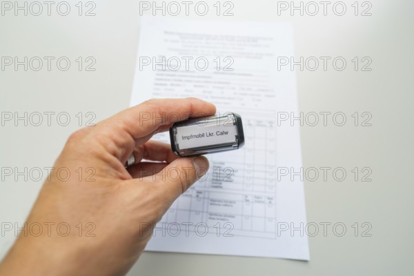 Close-up of a stamp in a hand over a form, Care Connect, vaccination kiosk for refugees, Calw, Germany