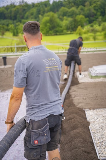 Two construction workers lay a hose on a roof with a view of the surrounding nature, roof greening, house construction, climate neutral