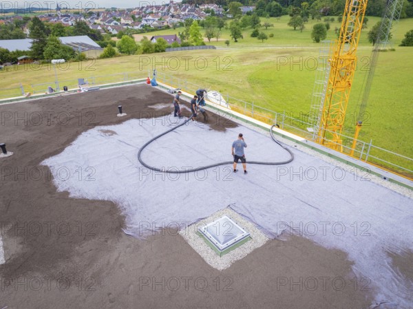 Workers attaching hoses to a roof next to an open field, roof greening, house construction, climate neutral