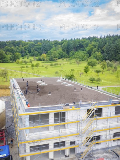Building shell with crane and workers, surrounded by trees and clear sky, green roof, house construction, climate neutral