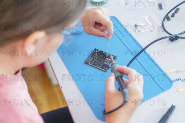Person wearing safety goggles soldering precisely on a printed circuit board on a blue surface
