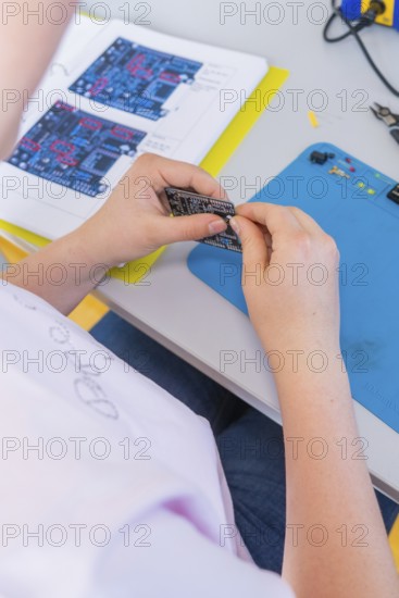 Person studying a circuit board and a manual on a table with a blue background