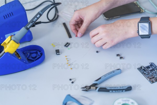 Working with electronic components on a table, soldering iron and hands clearly visible