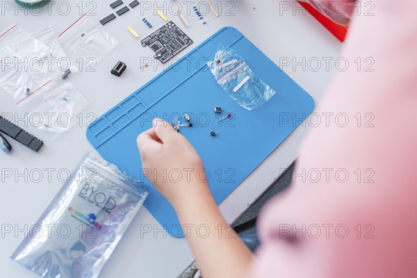 Person arranges electronic components on a blue pad with circuit board