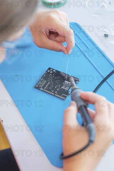 Person uses a soldering iron to work on a printed circuit board on a blue base