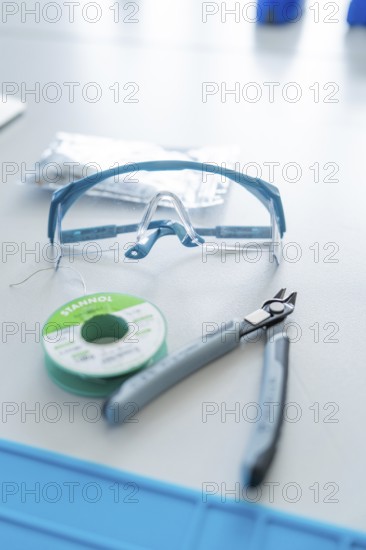 Safety goggles, pliers and solder on a table for electronics work