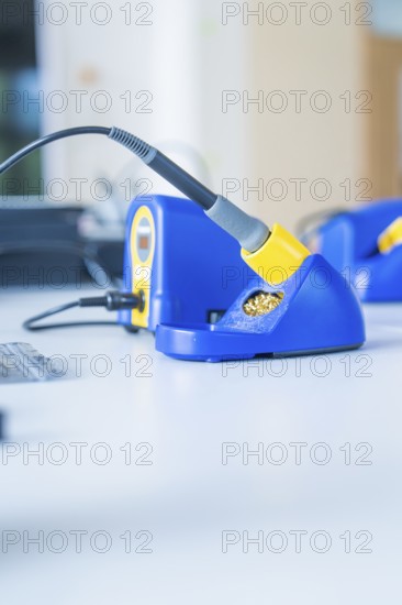 Close-up of a blue soldering iron on a workshop table with blurred background