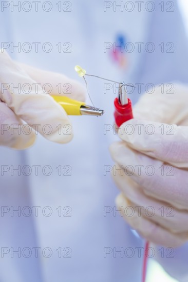Close-up of hands holding an LED and cables in an experiment, Battery Research, Nagold, Germany
