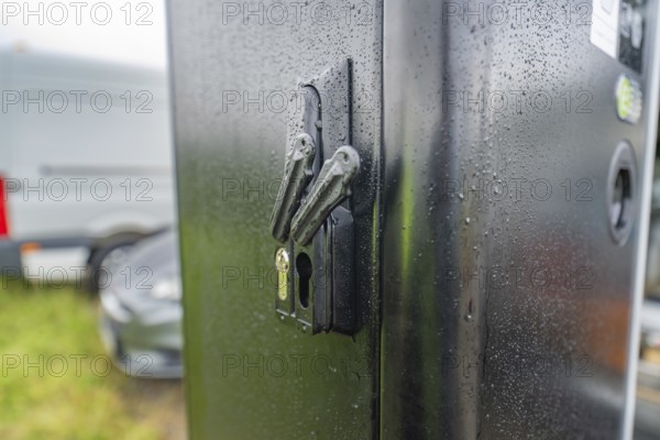 Security lock on a rain-soaked, black housing next to a parked car, installation of a charging station for electric cars, Calw, Germany