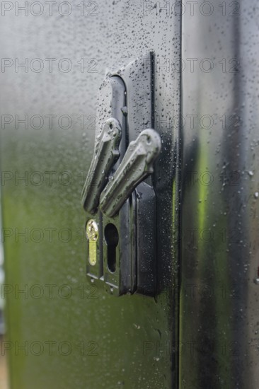 Wet lock on a black door with visible water droplets and reflected light, installation of a charging station for electric cars, Calw, Germany