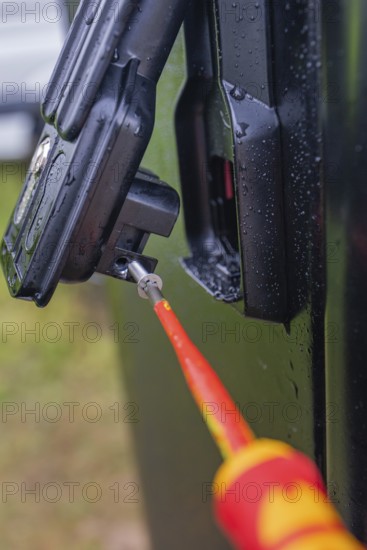 Close-up of a screwdriver attached to a black housing, covered with water droplets, assembly of a charging station for electric cars, Calw, Germany
