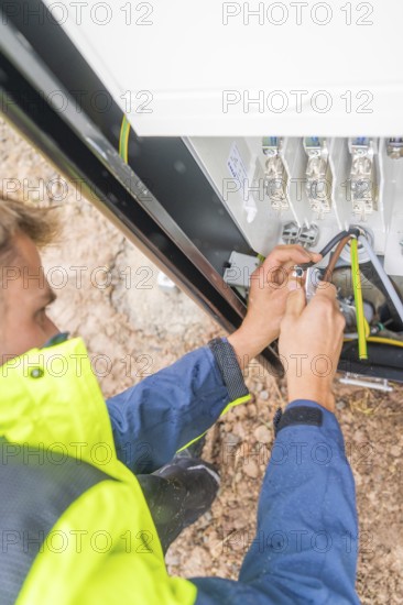 Worker fixing cables with tools in an electrical installation, assembly of a charging station for electric cars, Calw, Germany