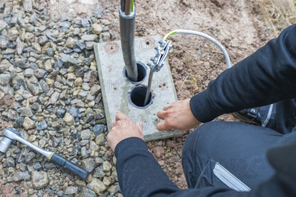Person installing cables on a ground plate on stony ground, installation of a charging station for electric cars, Calw, Germany