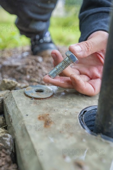 Hand holding a screw for mounting on a concrete base, installation of a charging station for electric cars, Calw, Germany