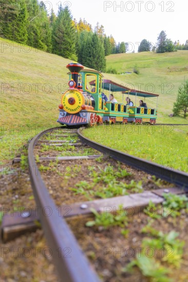 A colourful mini train moves through a green hilly landscape on narrow tracks, Retro Freizeitpark Poppeltal Riesenrutschbahn, Enzklösterle, Black Forest, Germany