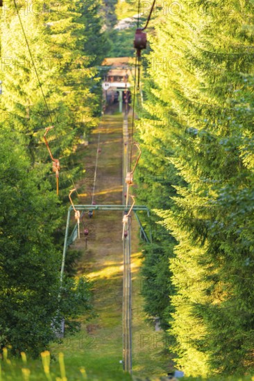 A ski lift moves quietly through a sunny forest surrounded by green trees, Retro Freizeitpark Poppeltal Riesenrutschbahn, Enzklösterle, Black Forest, Germany