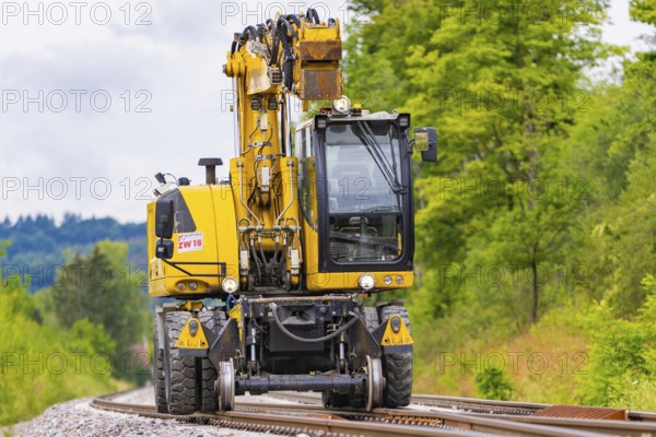 Large yellow construction machine on rails, surrounded by trees and greenery, grinding work on the Hermann Hesse railway, Ostelsheim, district of Calw, Germany