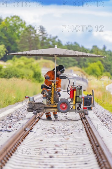 Worker using a machine on railway tracks under an umbrella, surrounded by greenery, grinding work on the Hermann Hesse railway, Ostelsheim, district of Calw, Germany
