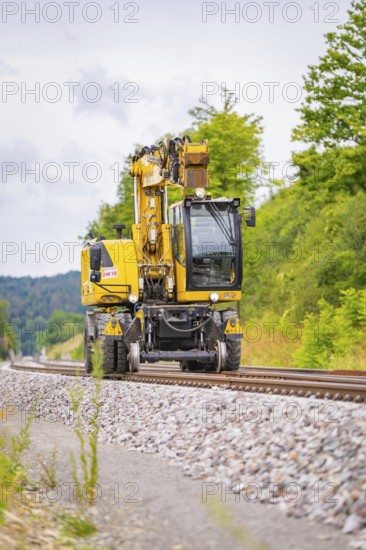 Yellow railway crane on railway tracks, surrounded by trees and ballast, grinding work on the Hermann Hesse railway, Ostelsheim, district of Calw, Germany