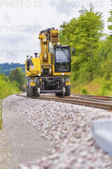 Large yellow machine runs on rails, surrounded by trees and clouds, grinding work on the Hermann Hesse railway, Ostelsheim, Calw district, Germany