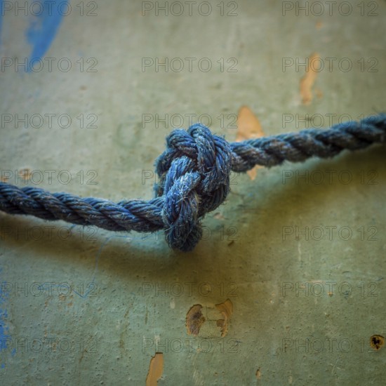 A close-up view reveals an intricately tied blue rope knot resting on a textured surface, highlighting the detailed craftsmanship involved in knot-making