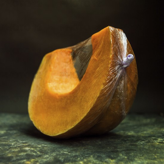A vibrant slice of pumpkin is displayed, encased in plastic wrap. The dark background enhances the pumpkin's rich orange hue, making it ideal for seasonal recipes or decorative purposes
