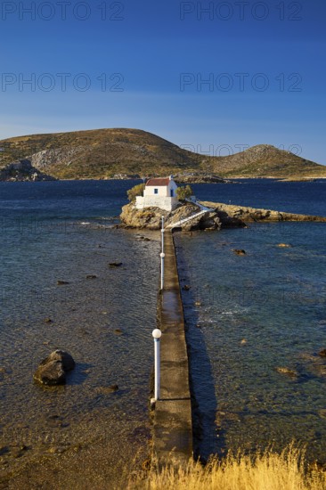 Long view of the chapel on the island with long jetty, surrounded by sea and blue landscape, chapel, church, Agios Isidoros, rocky islet, bay of Gourna, Kokkali, Leros, Dodecanese, Greek Islands, Greece